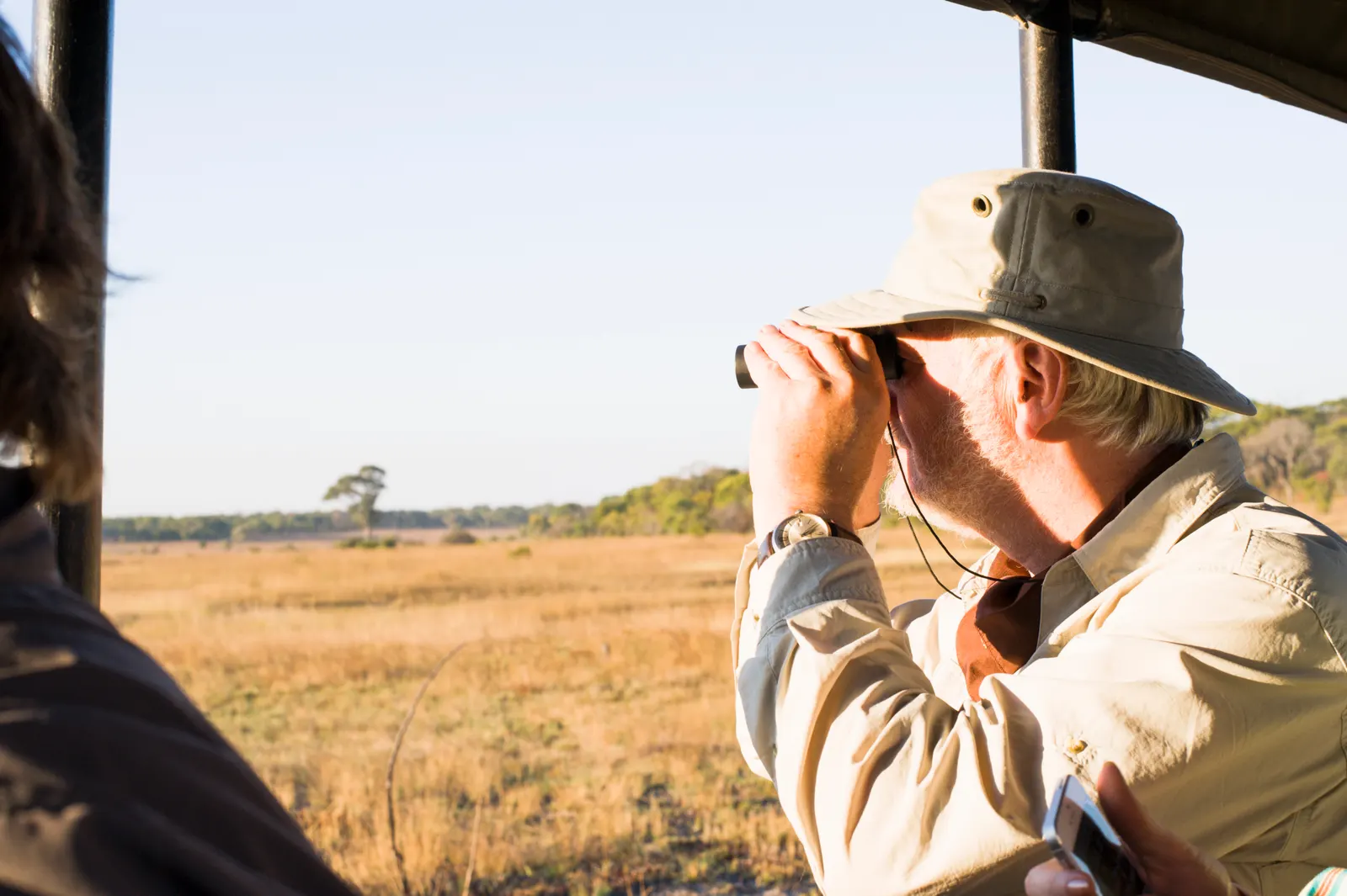 A guest scanning the plains with binoculars from a safari vehicle