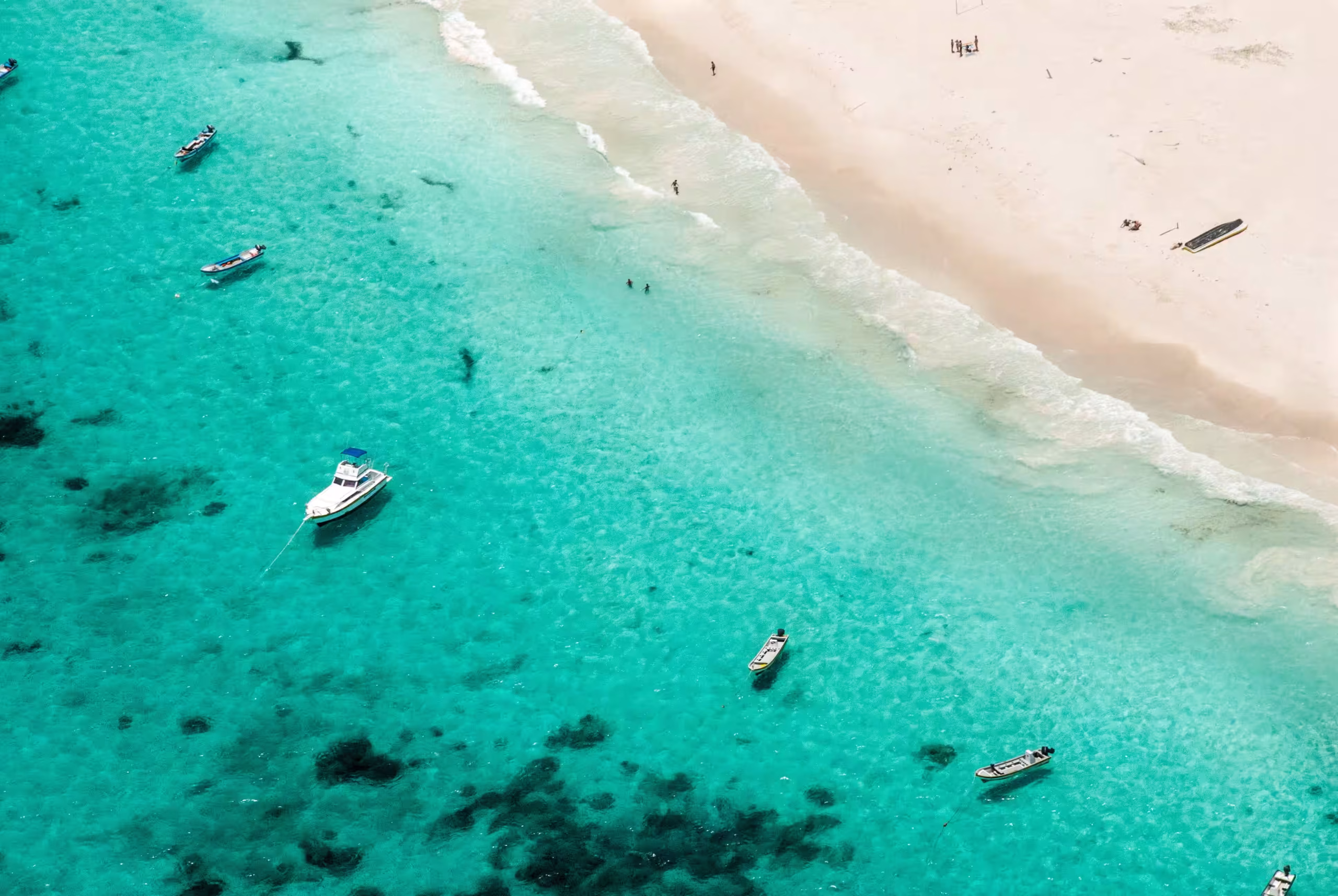 Boats at anchor over clear water off a beach