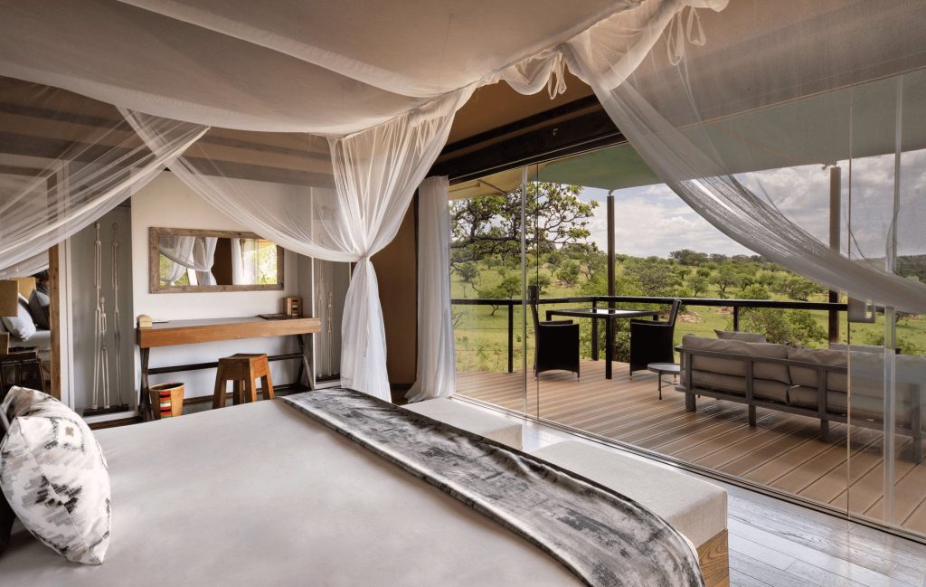 Lemala Kuria Hills Lodge: Suite bedroom with mosquito-net canopy bed and glass front opening to the private deck