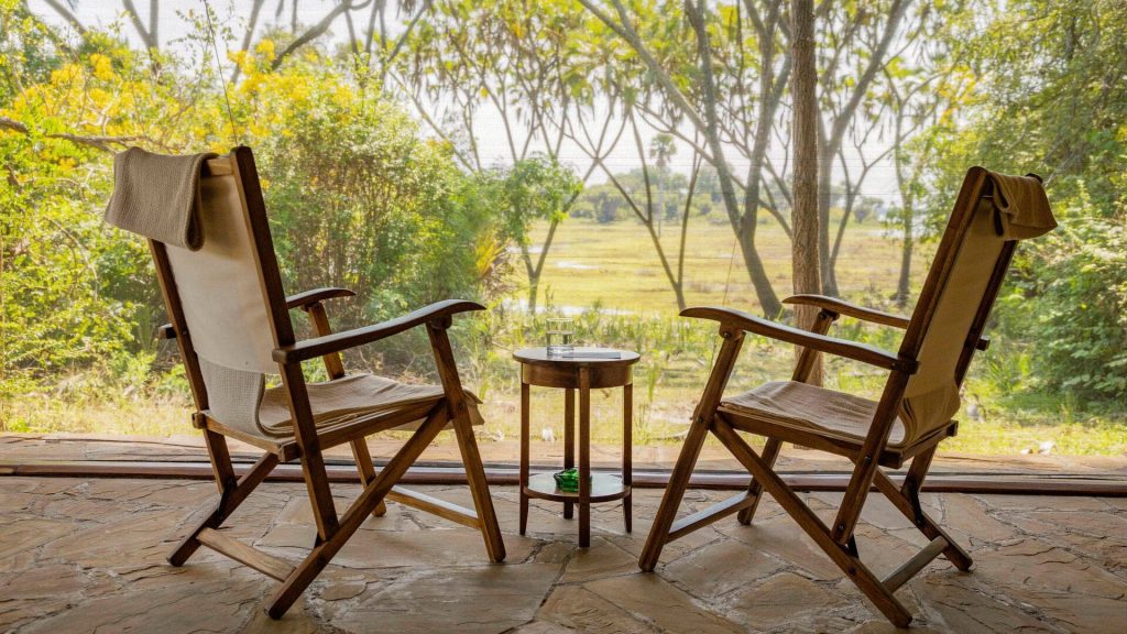 Roho ya Selous: Guest deck: two wooden chairs and a small table facing a green riverside view through trees