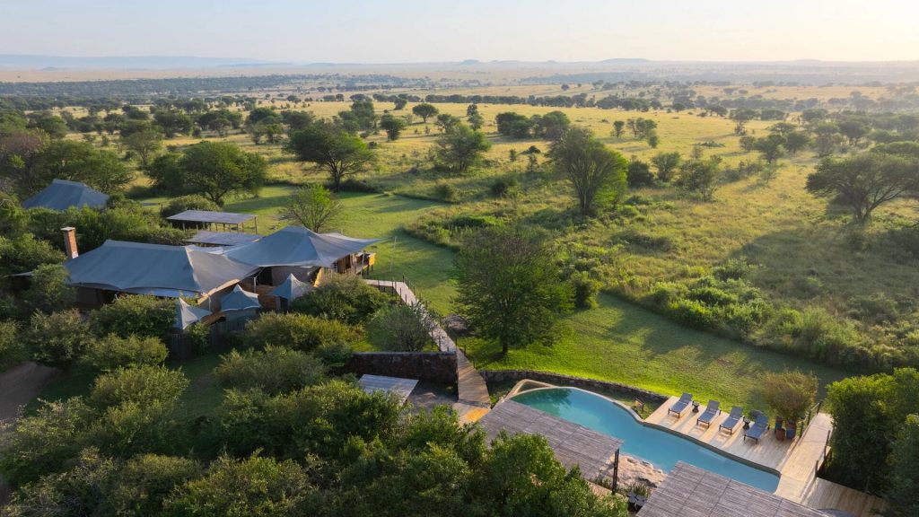 Aerial view of Sayari Camp: tented structures and swimming pool among trees overlooking the Serengeti plains